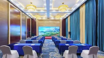 A conference room with rows of tables and chairs, a large screen at the front, and a chandelier.