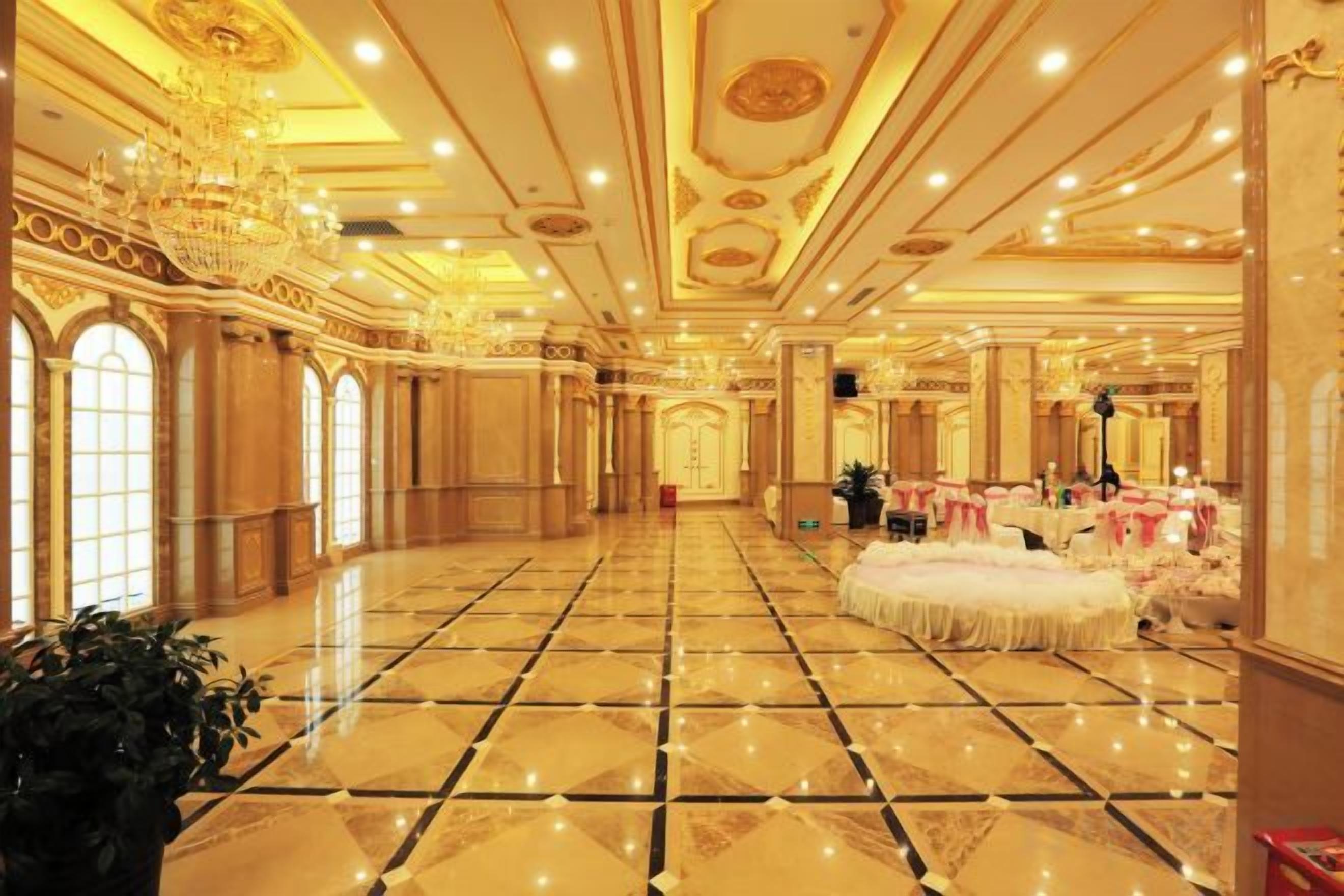 A spacious ballroom with a polished floor, ornate ceiling, and chandeliers.