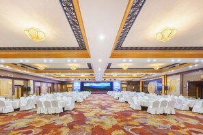 A banquet hall with rows of round tables, a carpeted floor, and a large screen at the front.