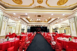 A banquet hall with tables arranged in rows, a stage at the front, and ornate ceiling decorations. - Korla Pear City Garden Hotel (Korla)