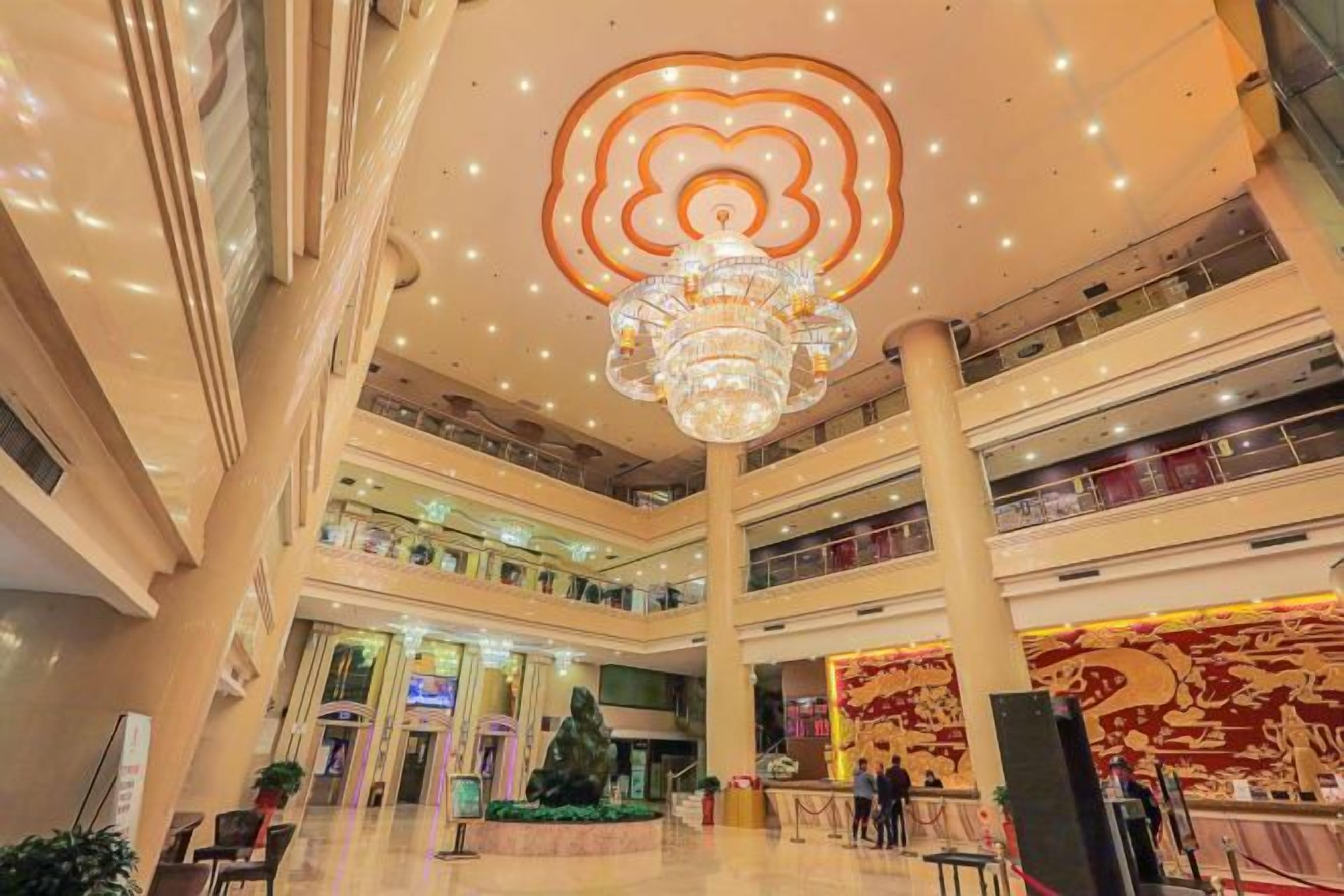 A multi-level shopping mall with a central atrium, a large chandelier, and a decorative wall.