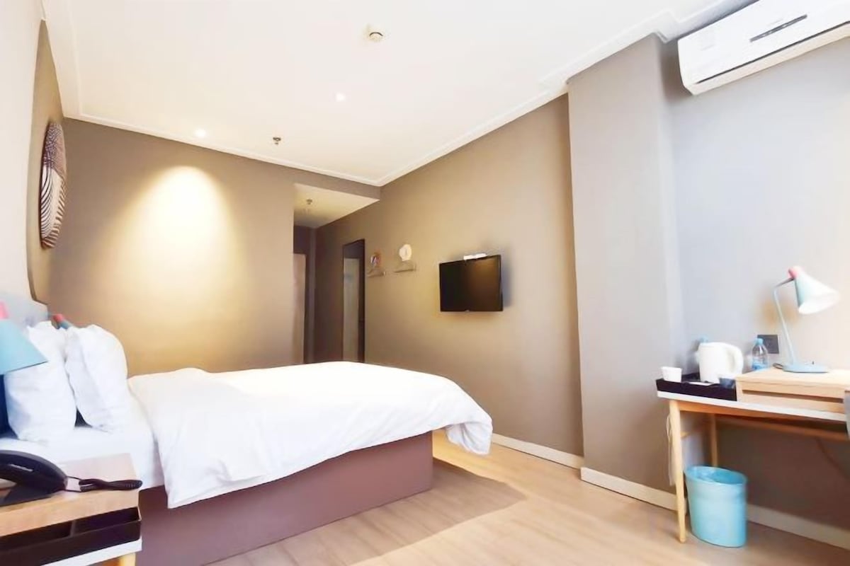 Ein Hotelzimmer mit einem Bett, einem Schreibtisch, einem Sessel, einem Fernseher und einer Wandklimaanlage.