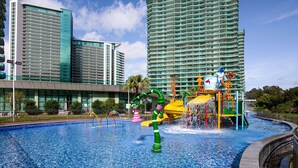 Una piscina con tobogán y zona de juegos, rodeada de modernos edificios altos.