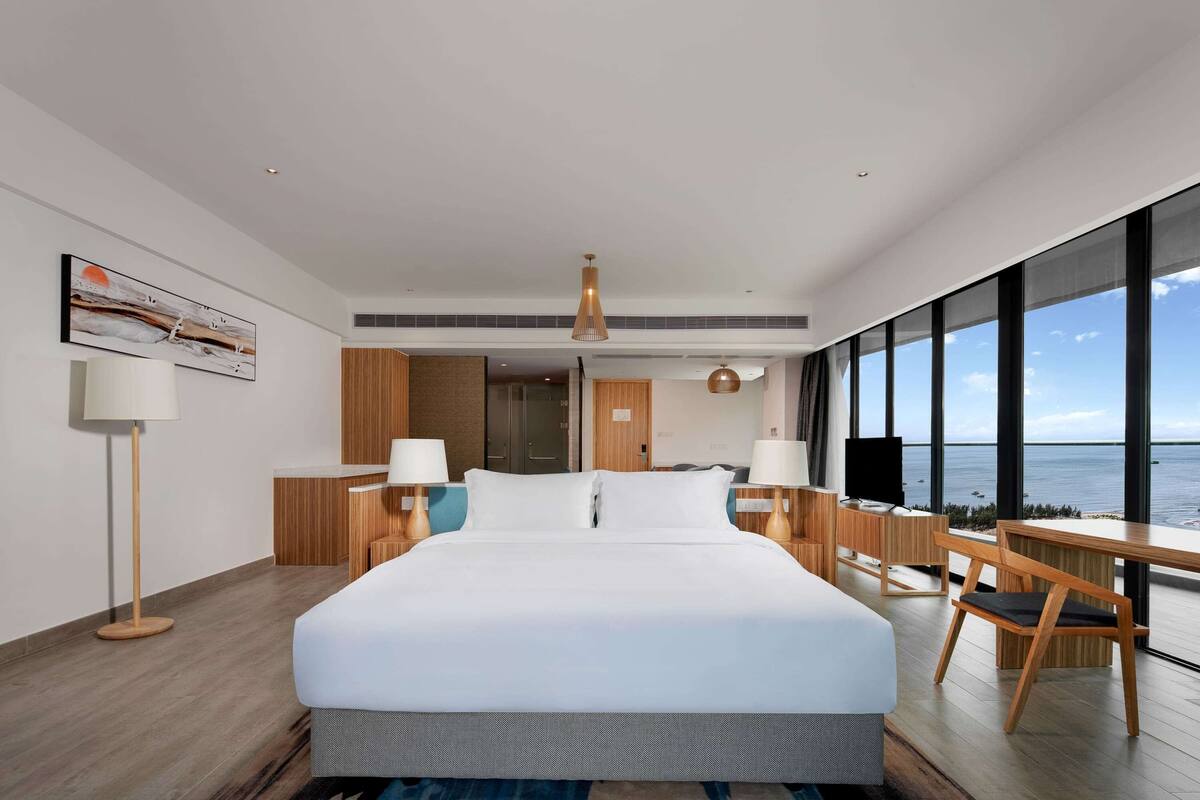A modern hotel room with a large bed, a desk, and a view of the ocean.