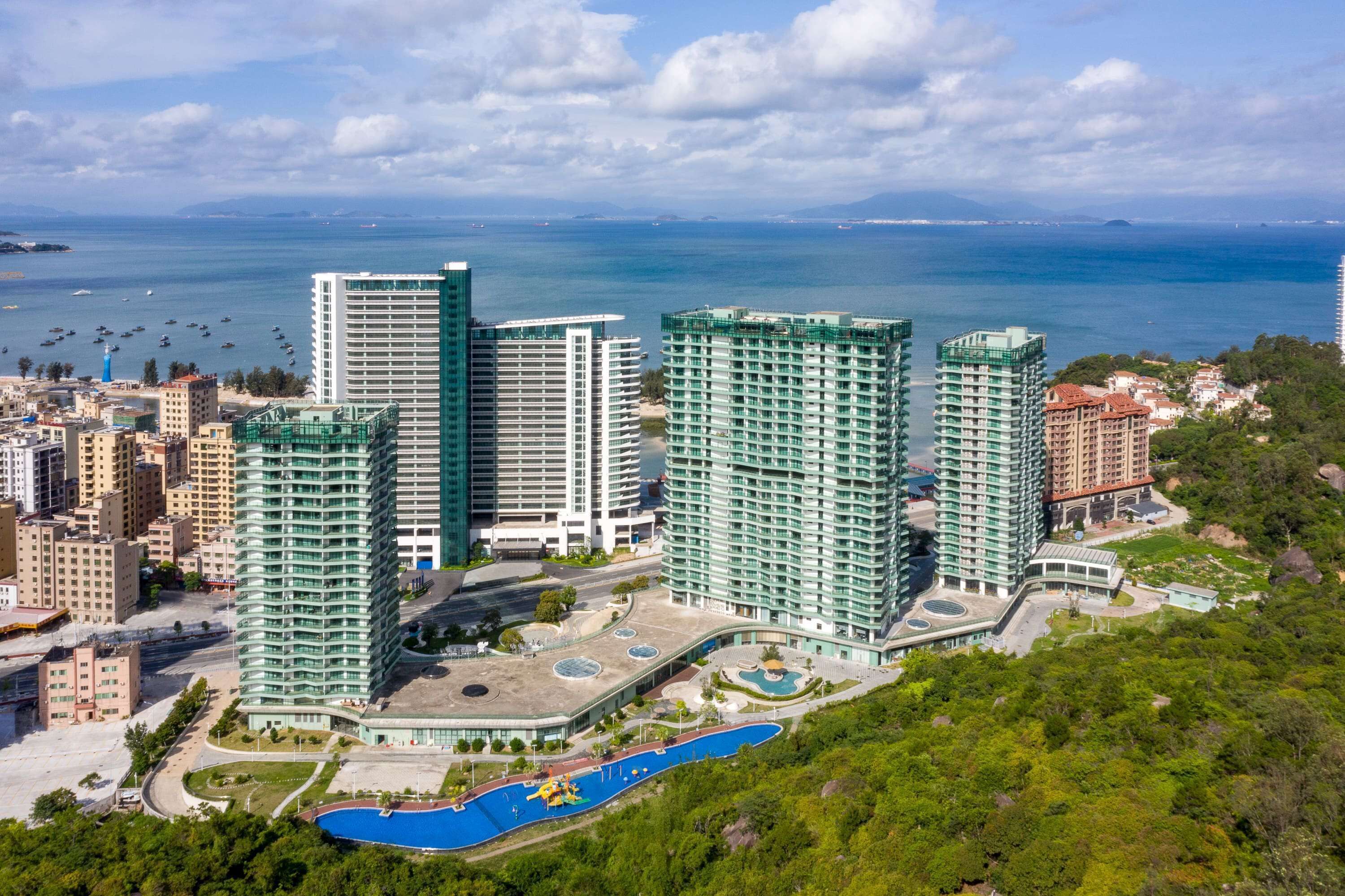 A high-rise hotel with multiple floors, a swimming pool, and a view of the sea.