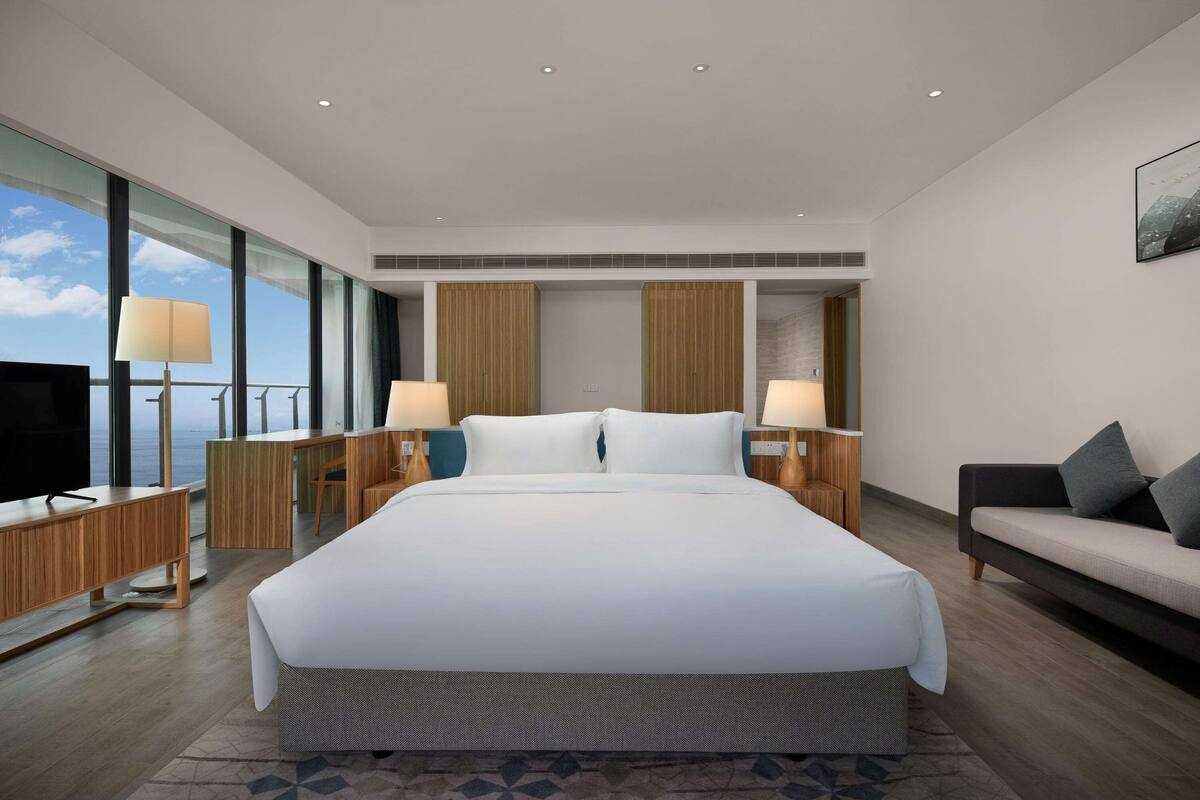 A modern hotel room with a large bed, a desk, a sofa, and a TV.