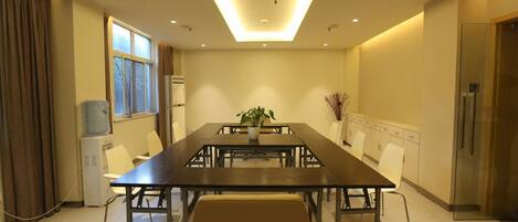 A conference room with a long table, chairs, a potted plant, a water dispenser, and a refrigerator.