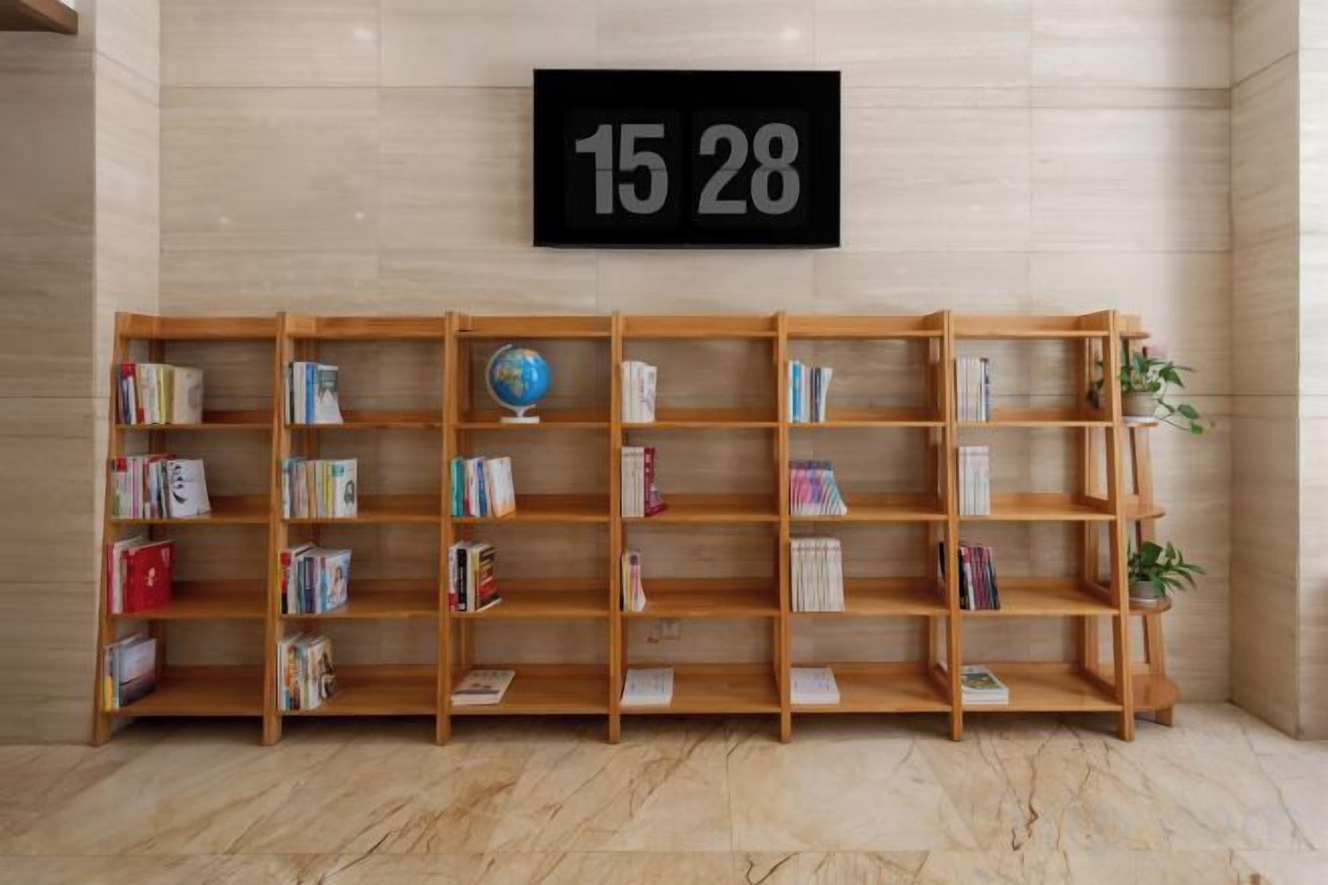 A row of wooden bookshelves with books and a globe, a black sign with numbers, and a potted plant.