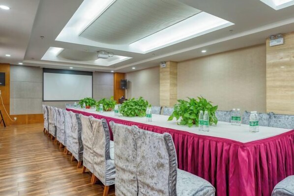 Un salón de conferencias con una larga mesa, sillas y una pantalla de proyector.