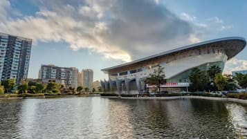 A modern building with a curved roof, a body of water in front, and a few trees.