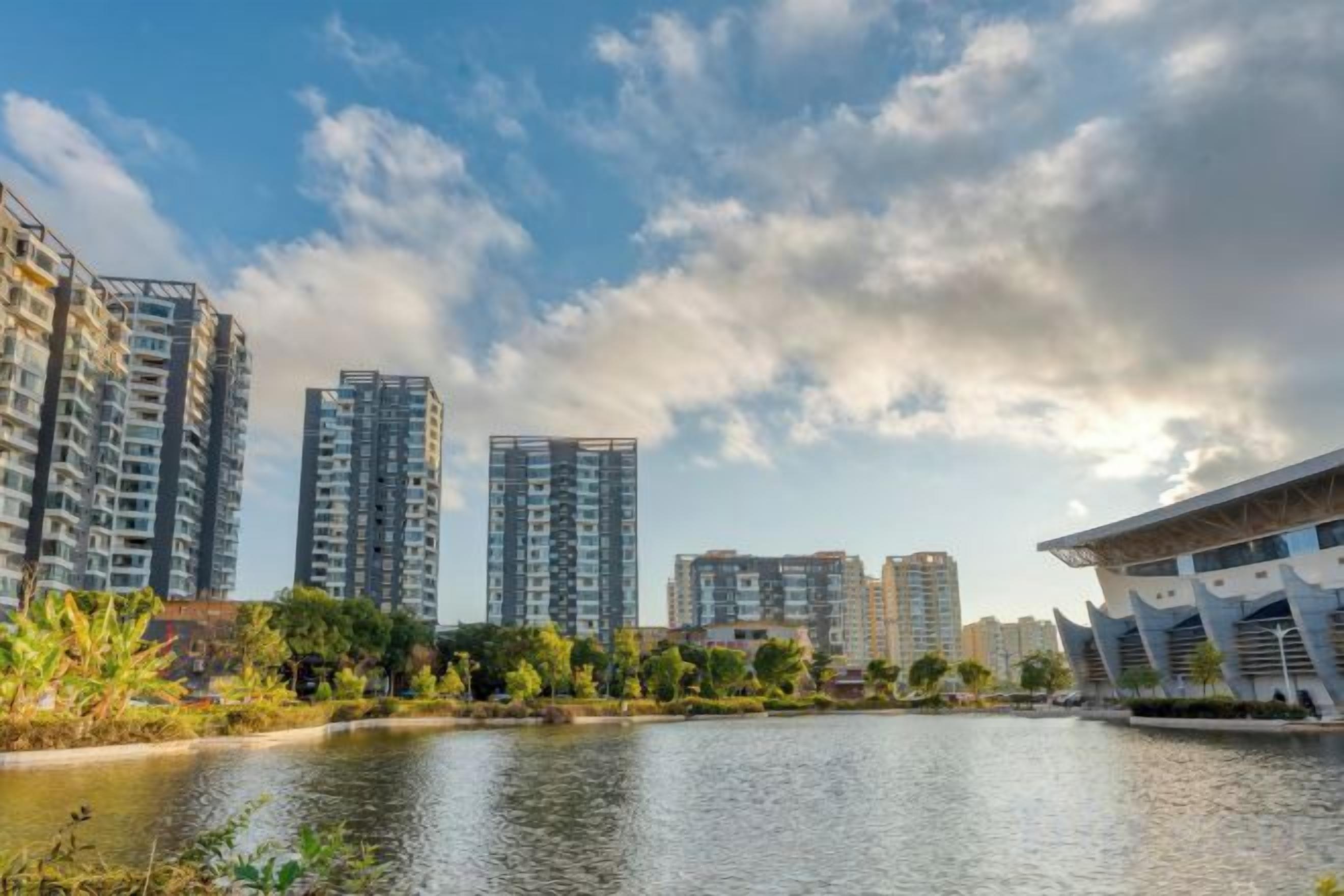 Un complexe immobilier moderne composé de plusieurs immeubles de grande hauteur, avec un plan d’eau et un design architectural unique, situé sur la droite.