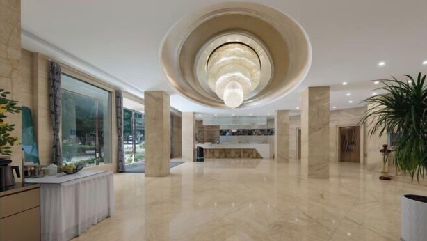 Um hall amplo com um lustre circular central, um balcão de recepção e uma grande janela.