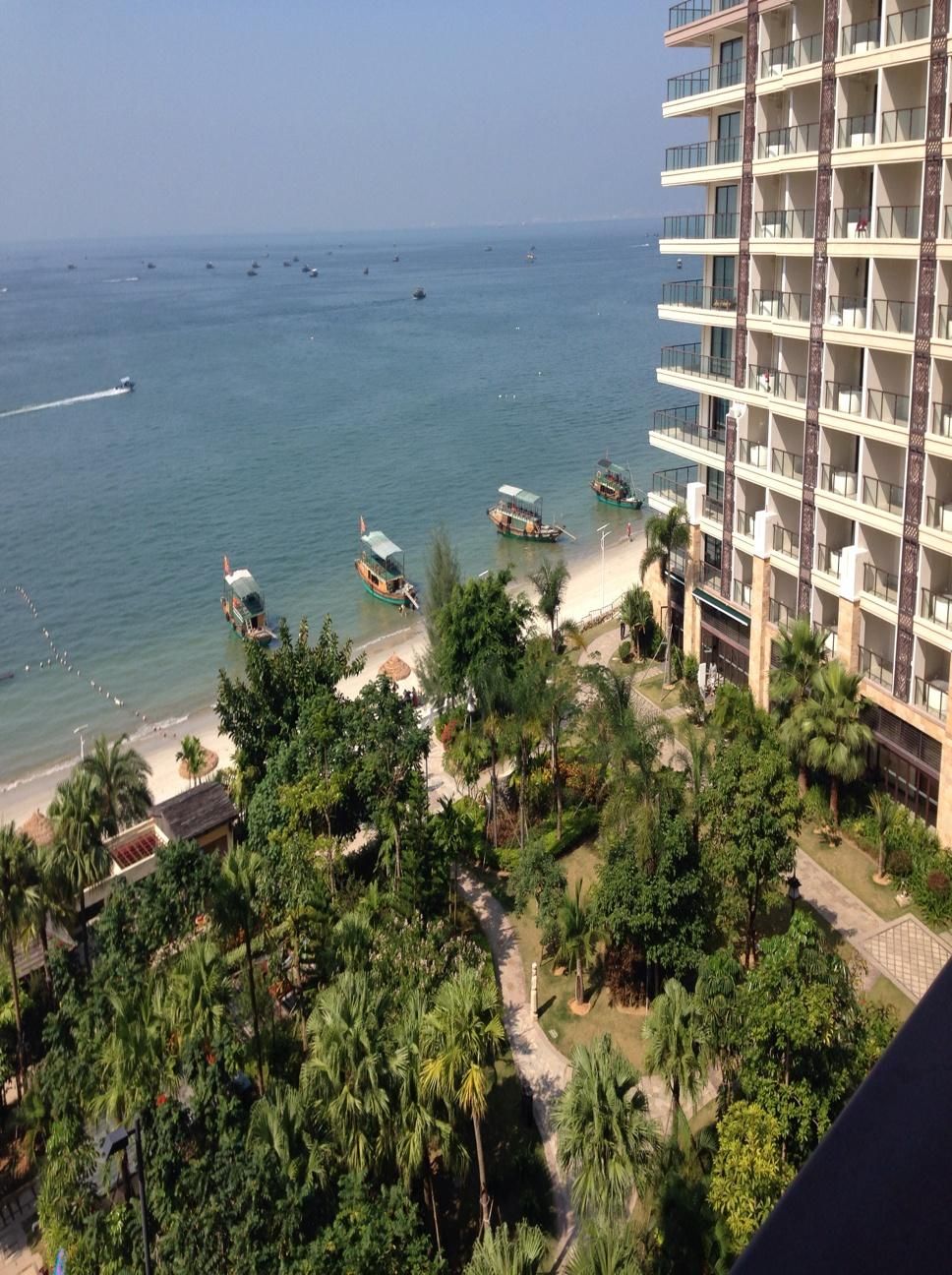 A high-rise hotel with multiple balconies overlooking a beach with boats and palm trees.