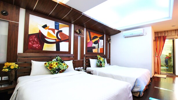 A hotel room with two beds, wooden headboards, abstract wall art, and a view of the outdoors. - Seashell Bay Hotel (Hengchun)