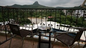 A balcony with two chairs and a table, overlooking a parking area and a mountain. - Seashell Bay Hotel (Hengchun)