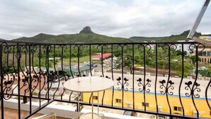 A balcony with a metal railing, a small round table, and a view of a green hill and buildings in the background. - Seashell Bay Hotel (Hengchun)