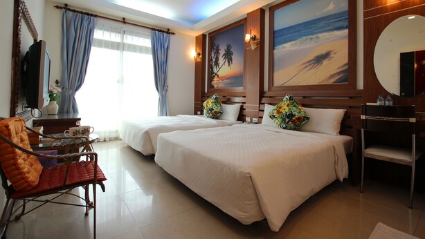 A hotel room with two beds, a desk with a chair, a large mirror, and artwork depicting a beach scene. - Seashell Bay Hotel (Hengchun)