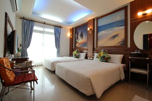 Une chambre d’hôtel avec deux lits, un bureau avec une chaise, un grand miroir et des œuvres d’art représentant une scène de plage.