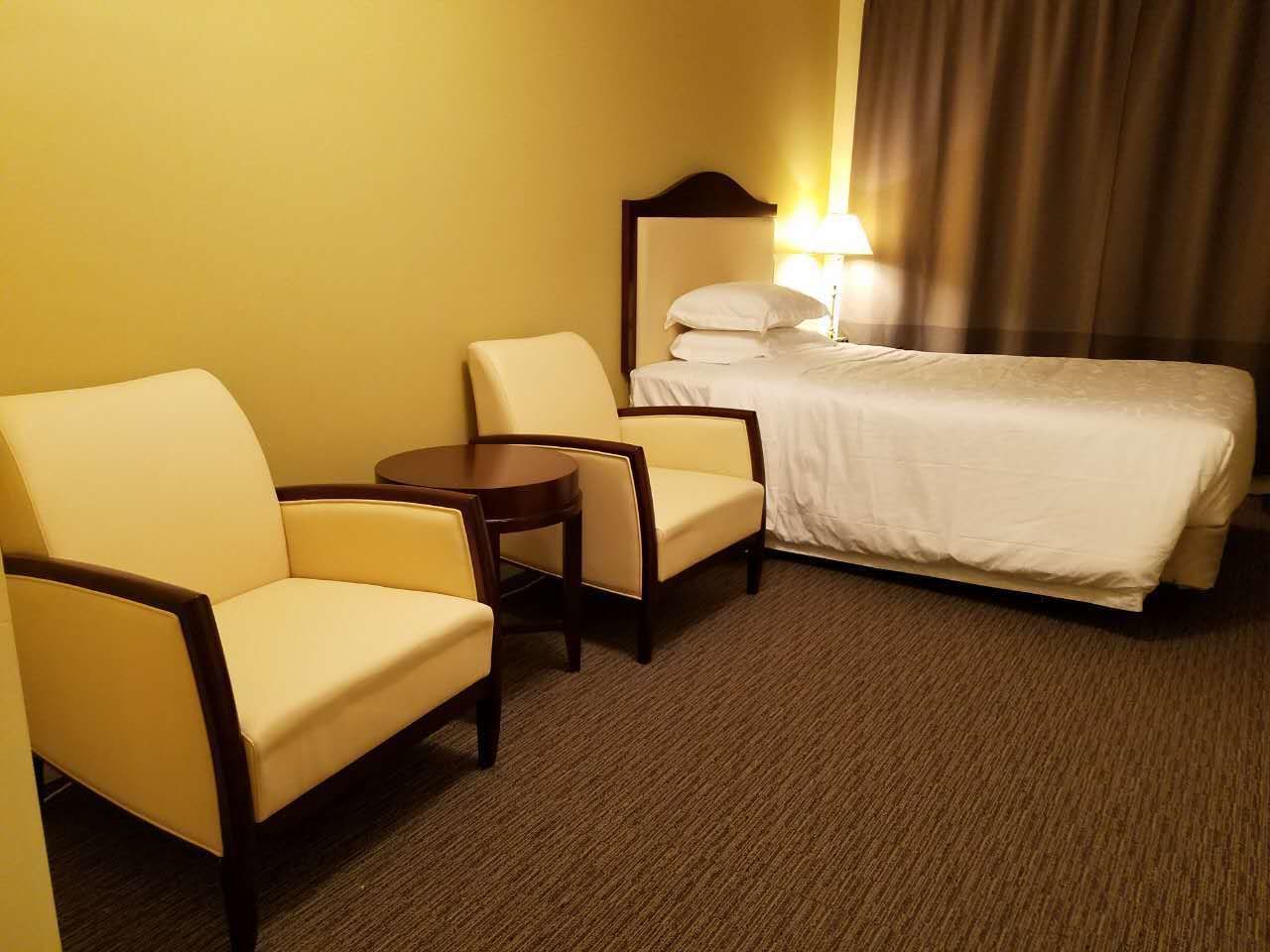 A hotel room with a bed, two armchairs, a small round table, and a lamp.