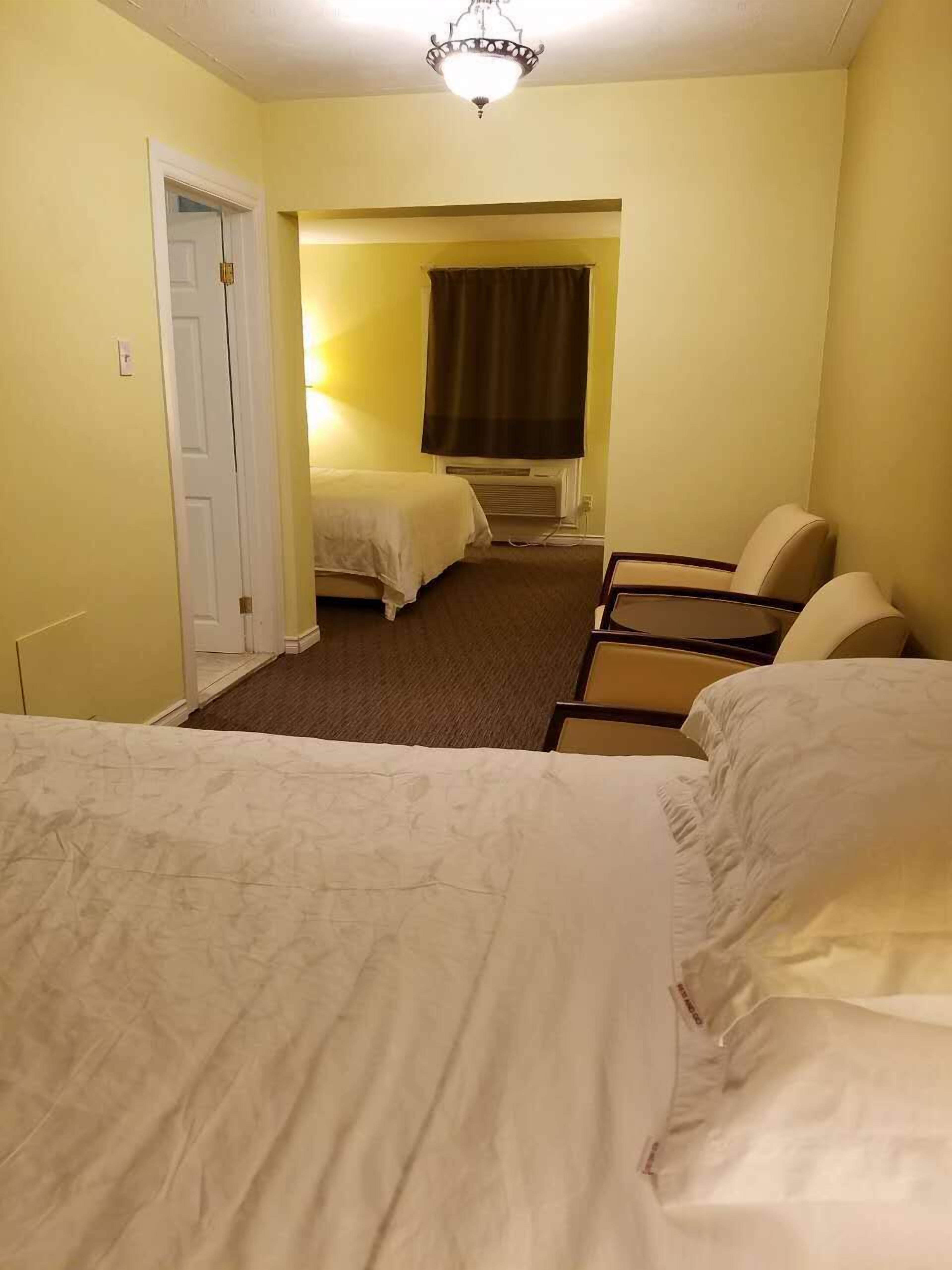 A hotel room with two beds, a small table, a chair, and a window with curtains.