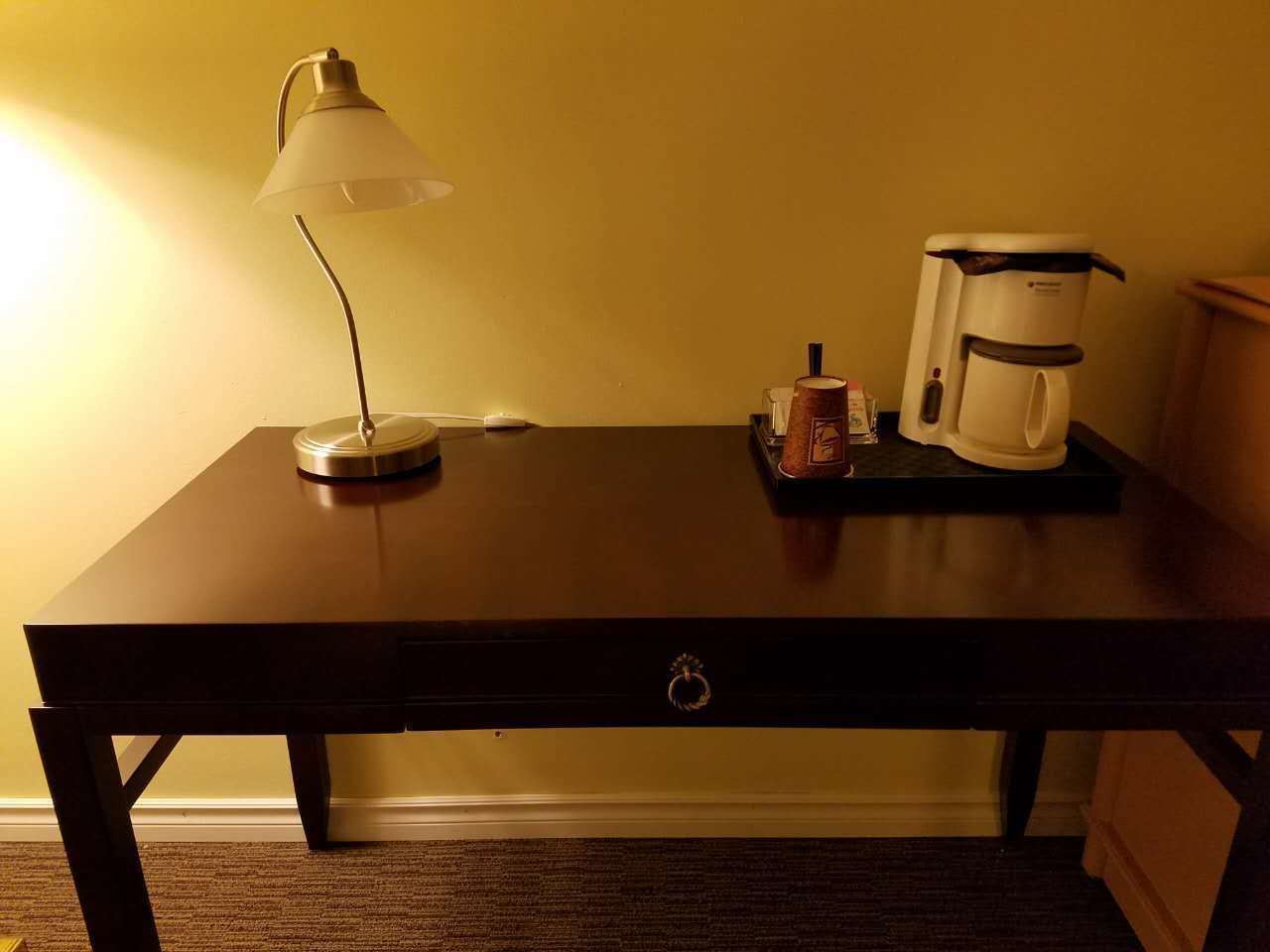 A wooden table with a lamp, a coffee maker, and a small box on it.