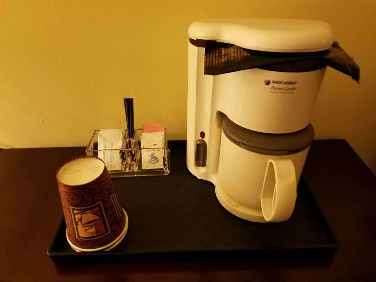 A coffee maker on a black tray with a disposable coffee cup and a tissue box.