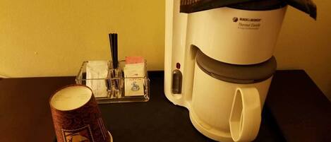 A coffee maker on a black tray with a disposable coffee cup and a tissue box.