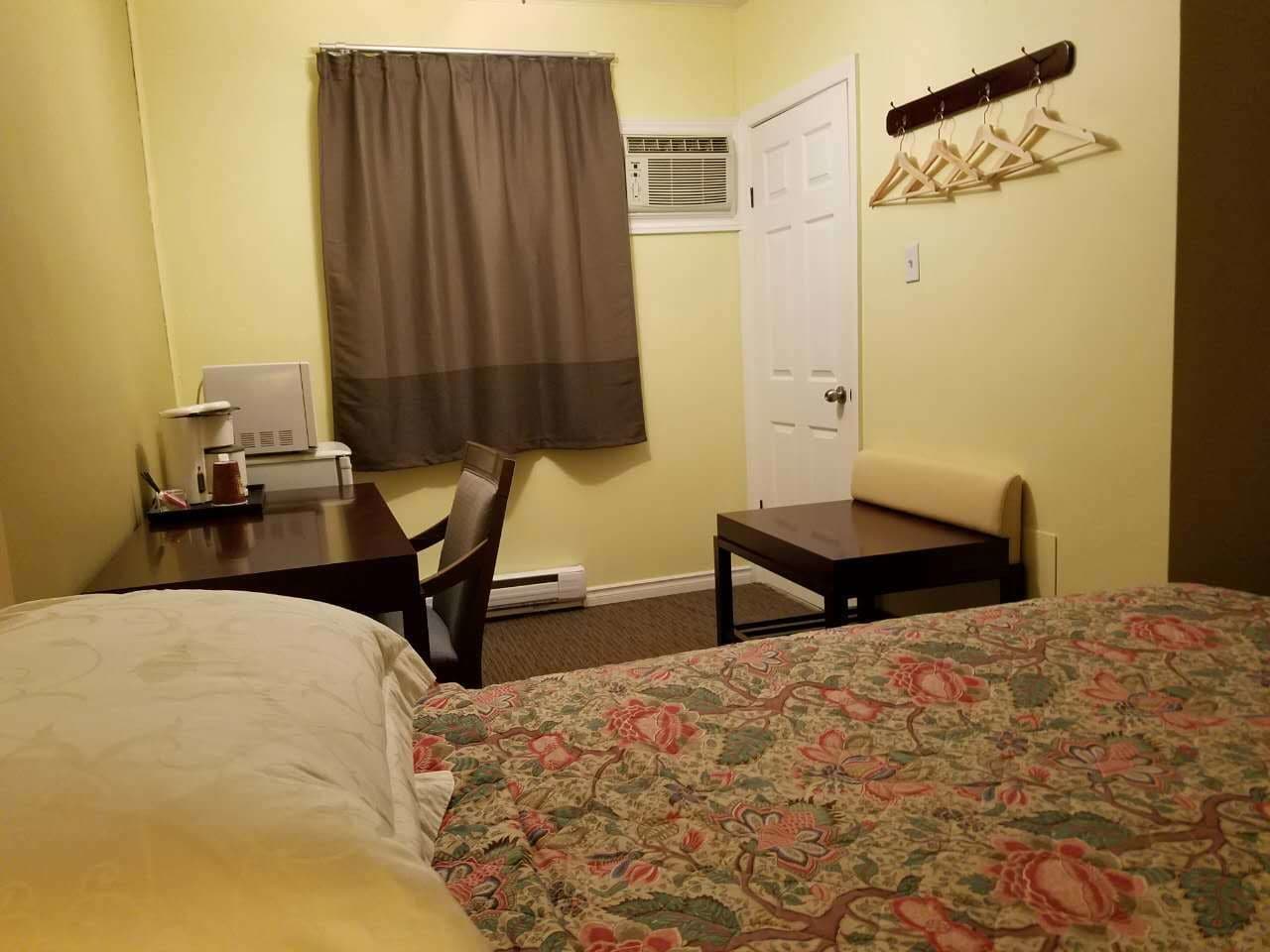 Habitación de hotel con cama, escritorio, silla, perchero y puerta.