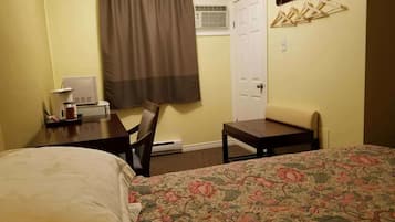 Habitación de hotel con cama, escritorio, silla, perchero y puerta.