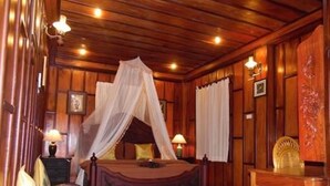 A wooden room with a bed, two bedside tables with lamps, a chair, and a small table. - Villa Senesouk (Luang Prabang)