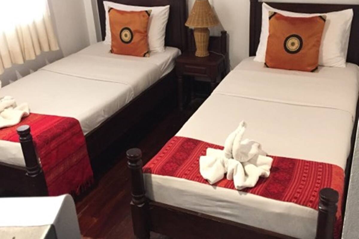 A hotel room with two single beds, wooden headboards, white bedding, and a red and white patterned bedspread.