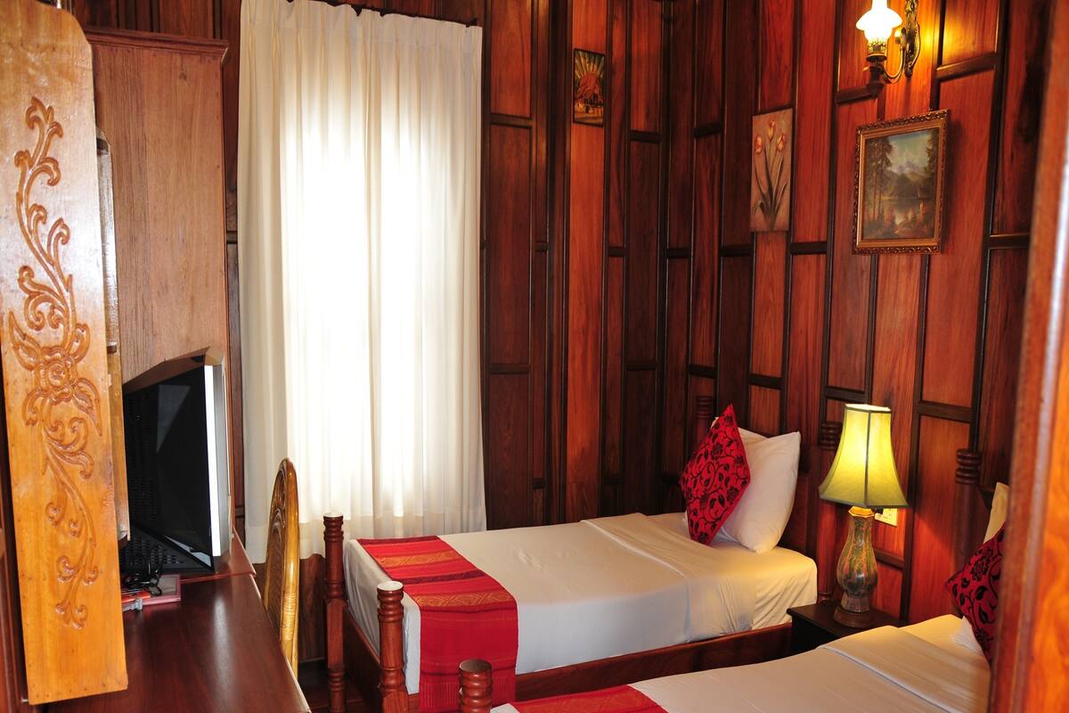 A hotel room with two wooden beds, a desk with a television, and a wooden wardrobe.