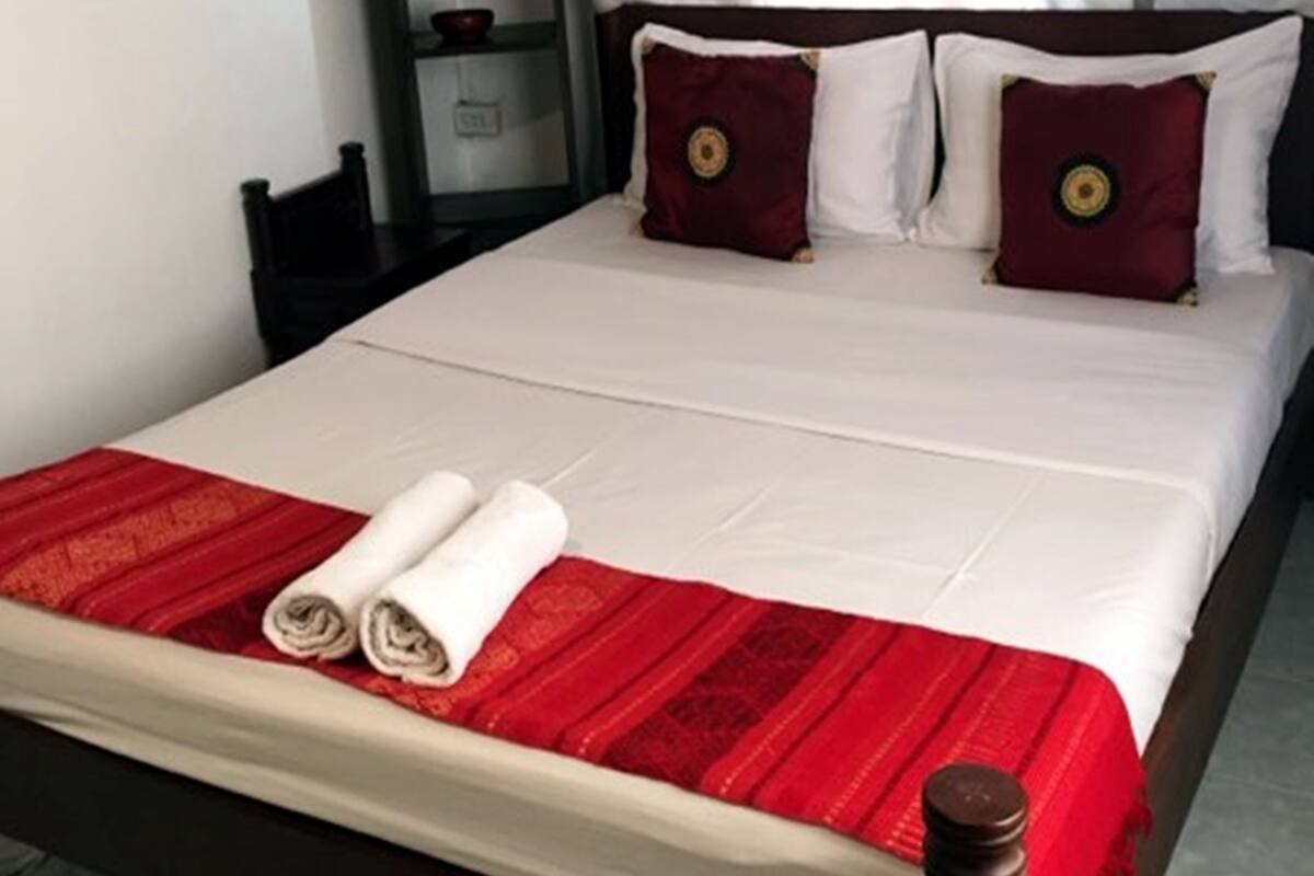 A neatly made bed with white and red bedding, a wooden headboard, and a small shelf with decorative items.