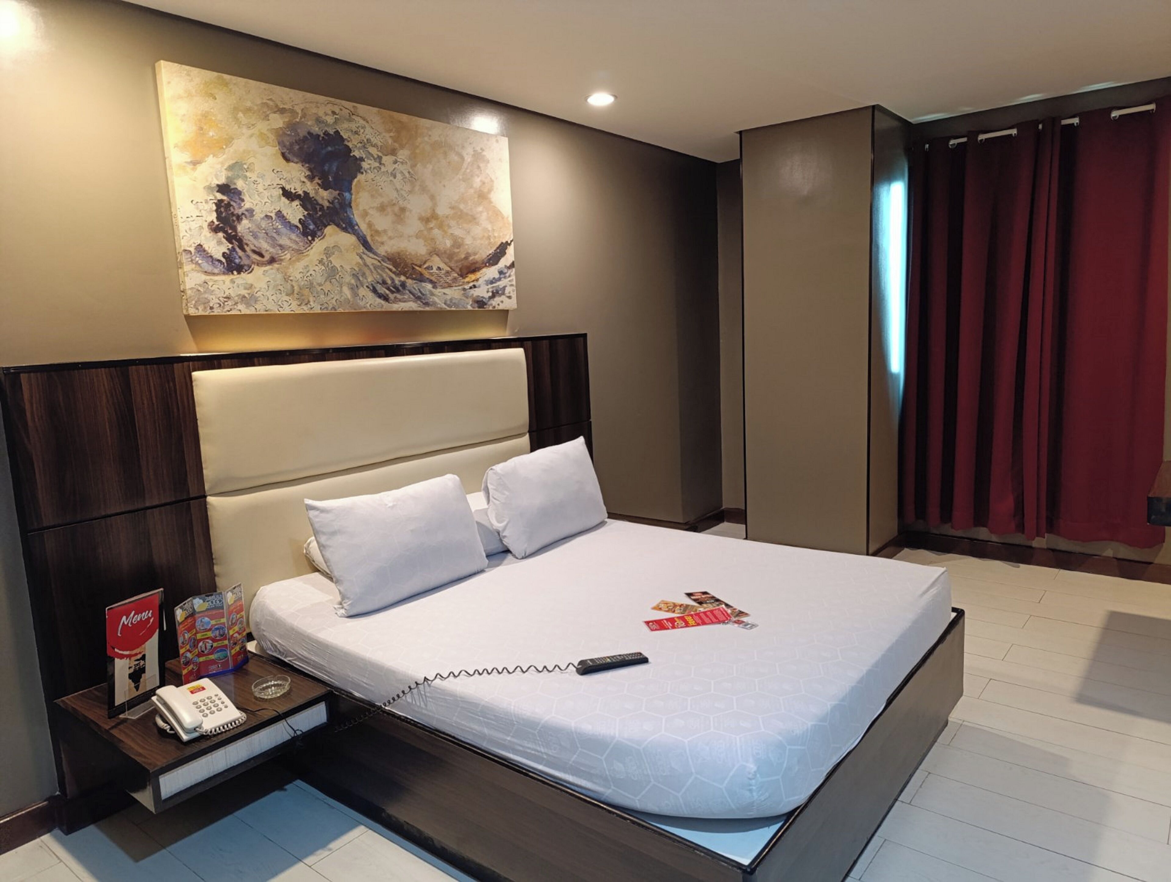A modern hotel room with a large bed, a headboard, a bedside table with a phone, and a painting on the wall.