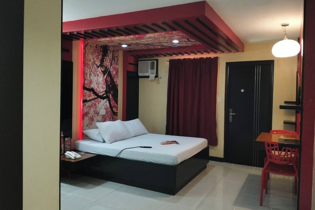 A bedroom with a bed, a desk, a chair, a wardrobe, and a red curtain.
