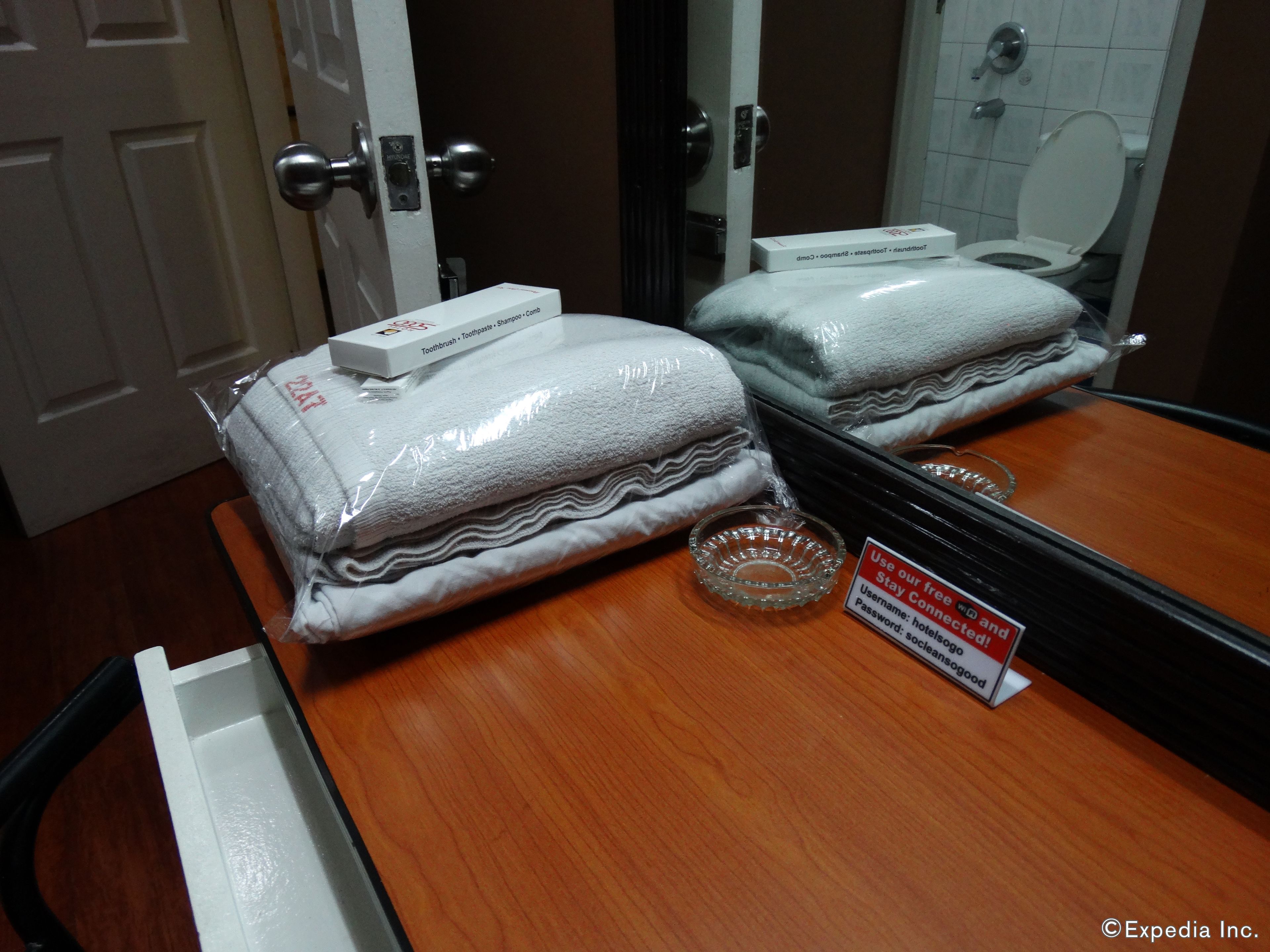 Une salle de bain d’hôtel avec un miroir, des toilettes et un lavabo. Des serviettes et un dentifrice se trouvent dans un sac en plastique sur le comptoir.