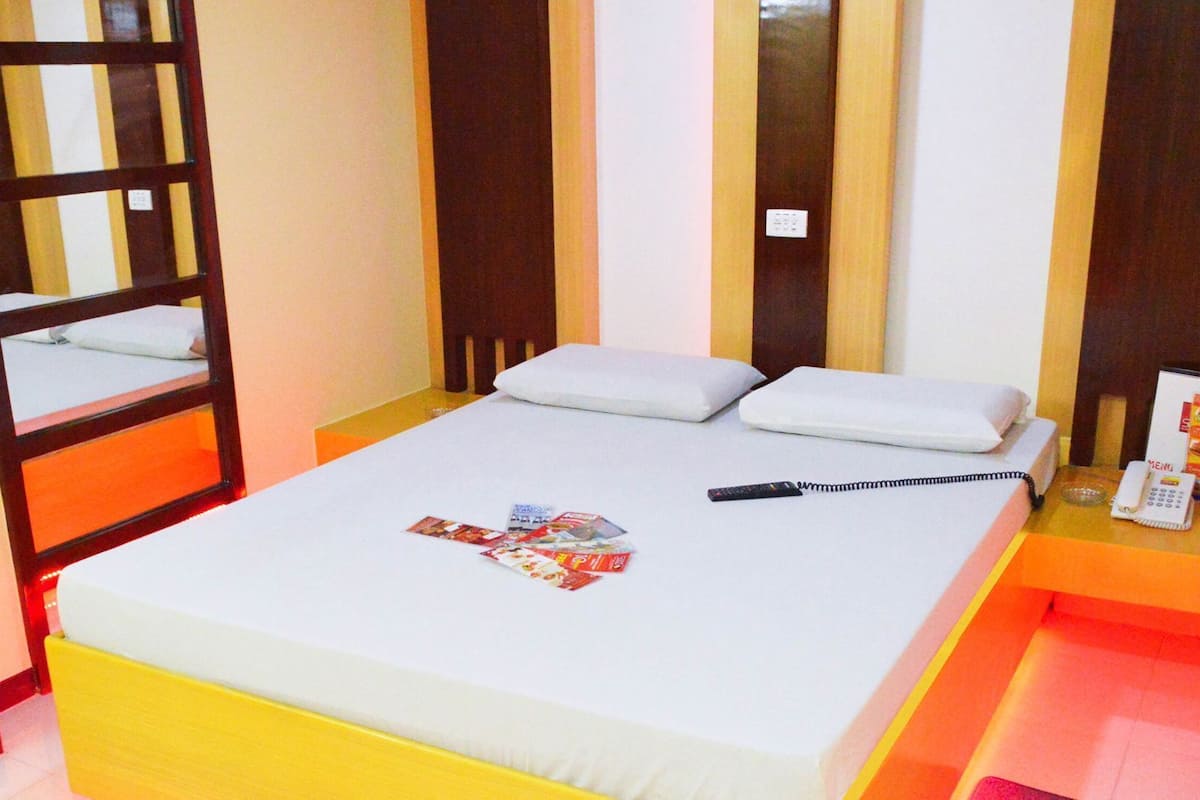 A hotel room with a bed, a bedside table with a phone, and a mirror.