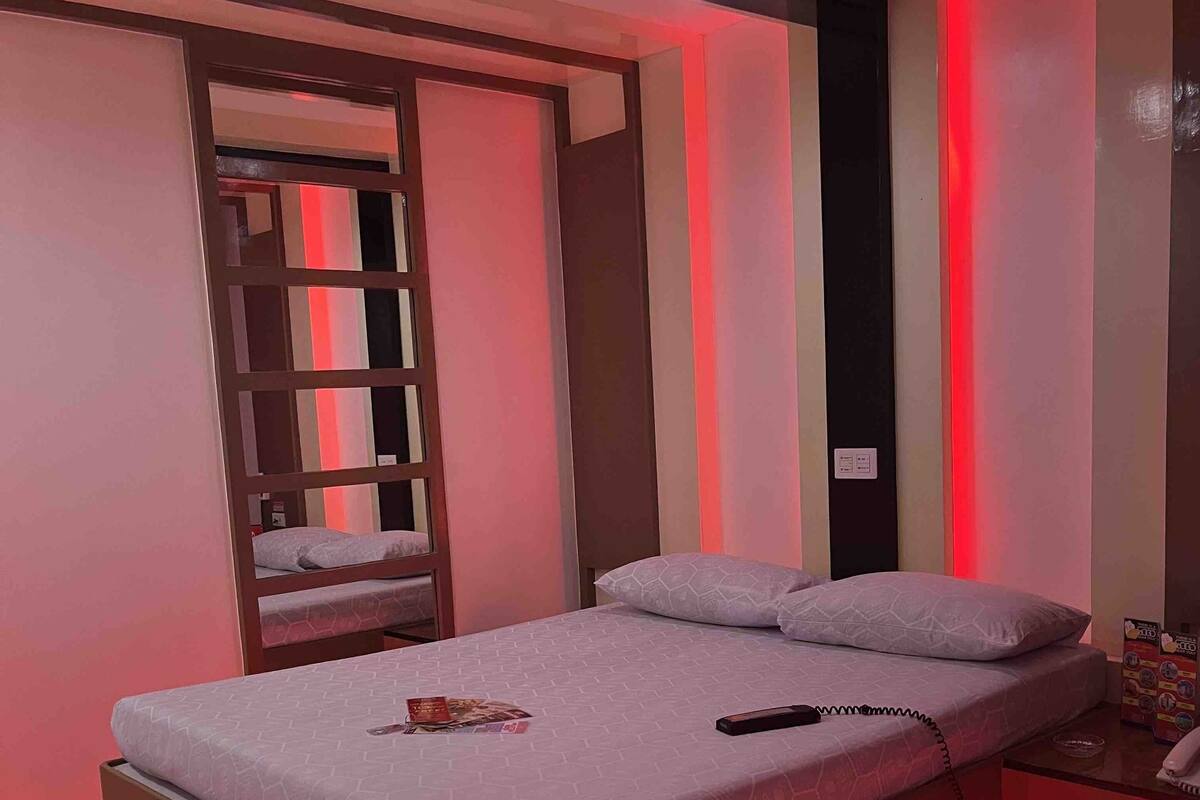A modern bedroom with a bed, a nightstand, and a red LED light strip along the bed's edge.