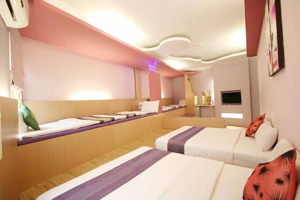 A hotel room with two beds, a built-in bench, a flat-screen TV, and a ceiling light fixture.