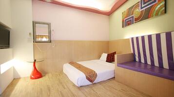A hotel room with a bed, a red vase, a television, and a wall with colorful artwork.