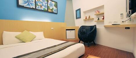 A hotel room with a bed, a chair, a desk, and a shelf with decorative items.