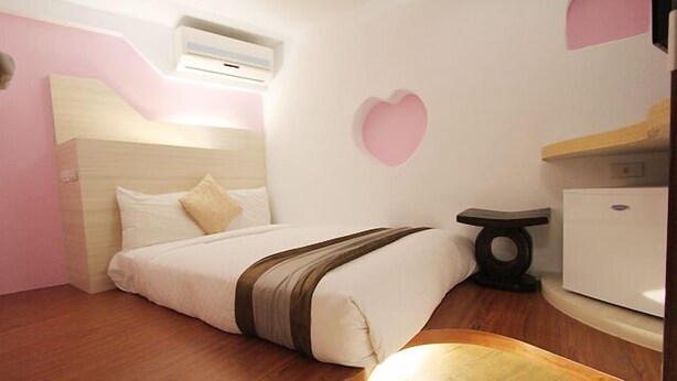 A bedroom with a bed, a bedside table, a dresser, and a wall-mounted air conditioner. - Kenting Hostel (Hengchun)