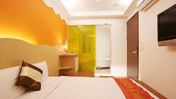 A hotel room with a bed, a TV, a bathroom visible through an open door, and a red carpet.
