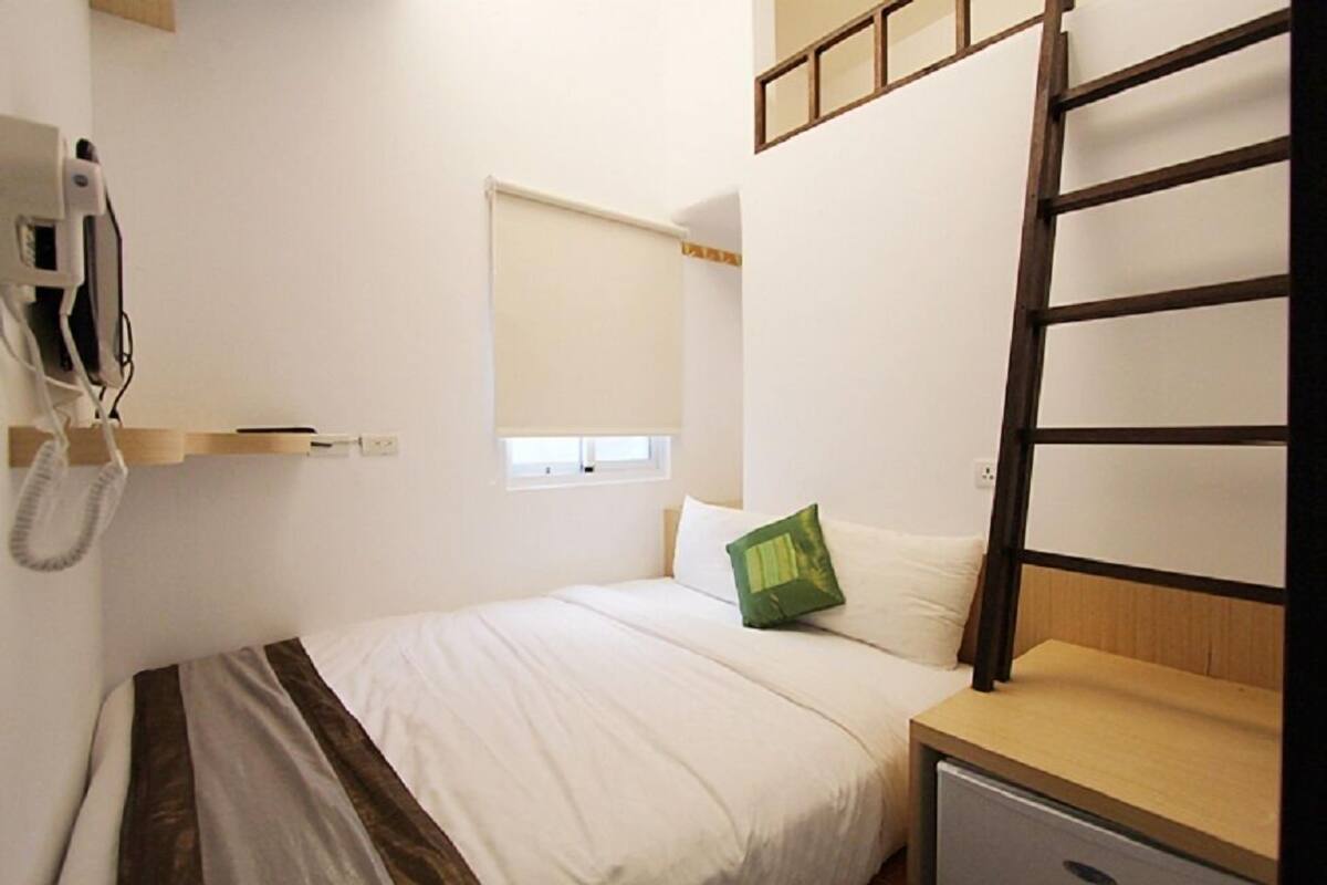 A small, single-bed room with a wooden headboard, a bedside table, a telephone, and a window with a blind.