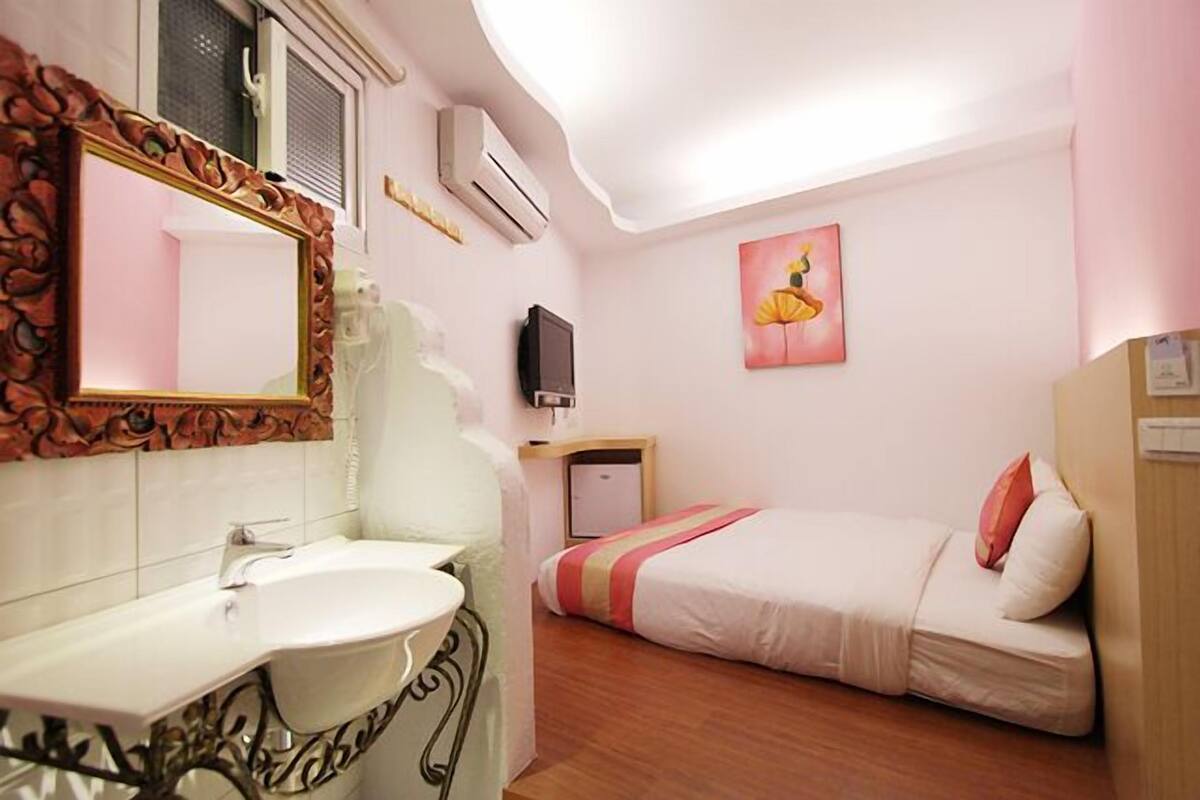 A bedroom with a bed, a bedside table, a TV, and a mirror.