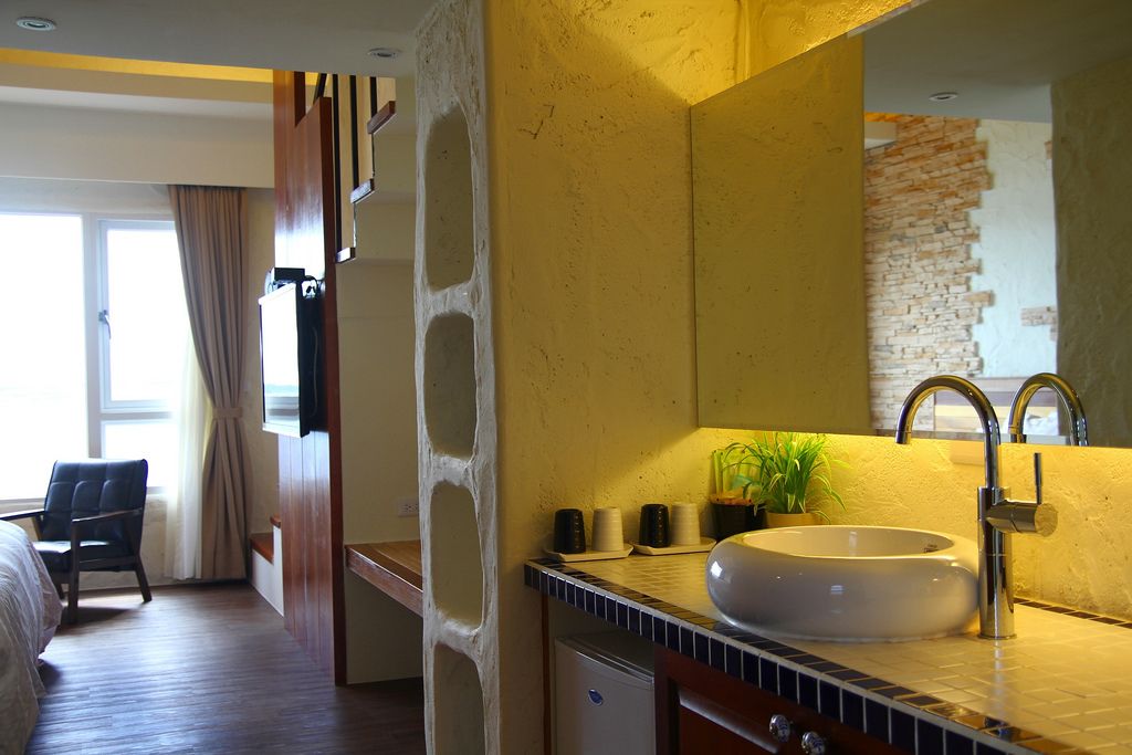 A hotel room with a large oval sink, a mirror, a potted plant, and a bed.