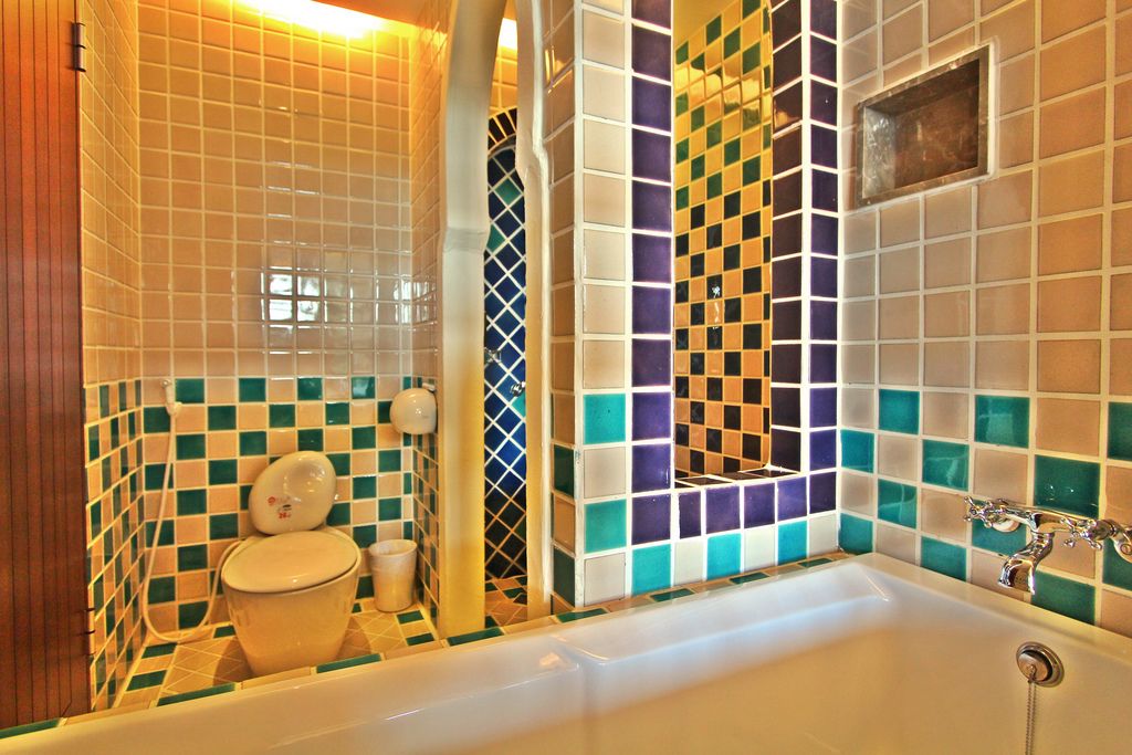 A bathroom with a bathtub, toilet, and sink. The walls are tiled with a checkered pattern.