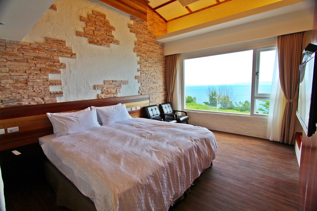 A hotel room with a large bed, a view of the sea, and a brick wall.