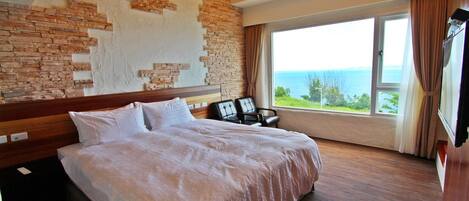 A hotel room with a large bed, a view of the sea, and a brick wall.