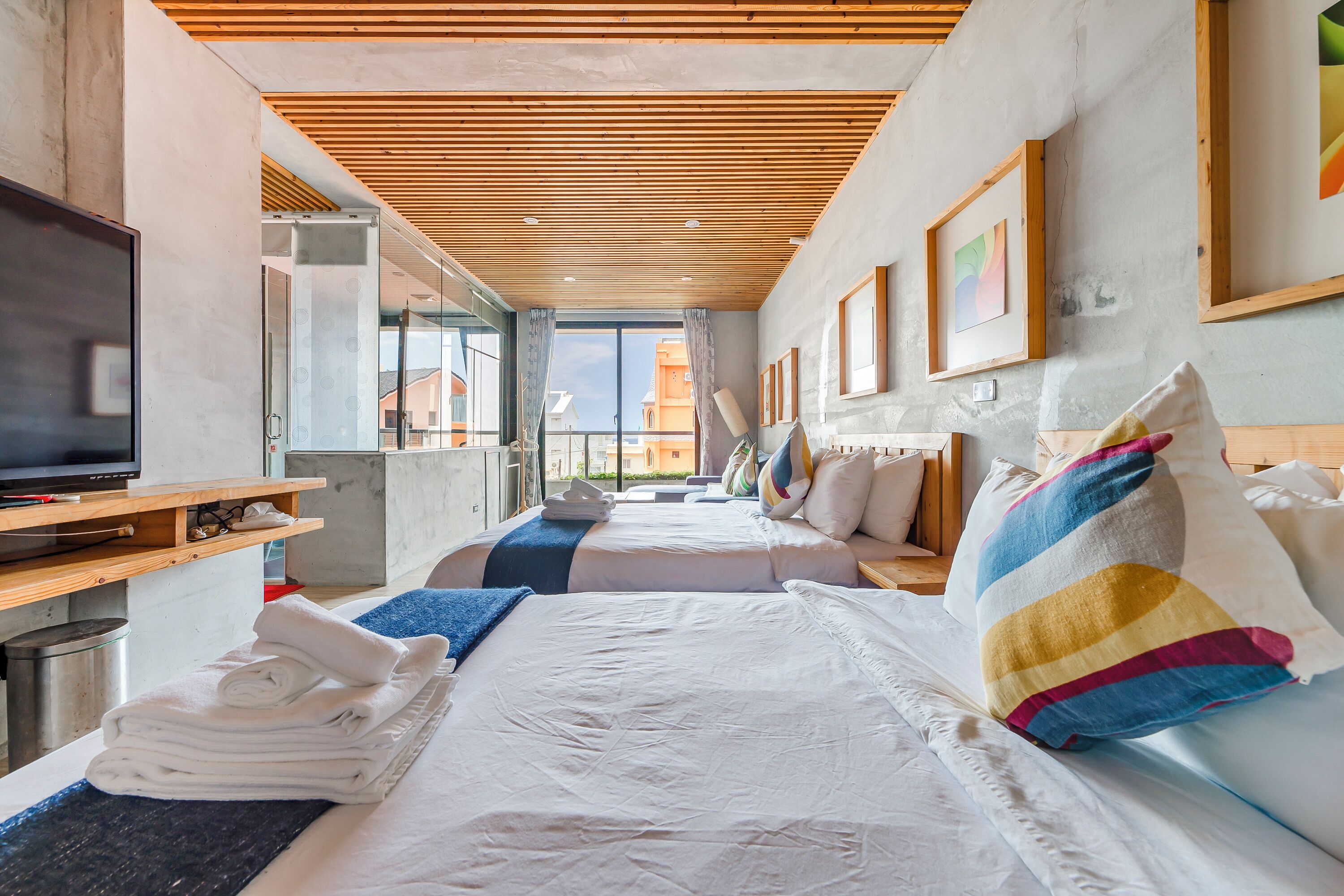 Une chambre d’hôtel avec deux lits, une télévision et une vue sur les bâtiments, grâce à de grandes fenêtres.